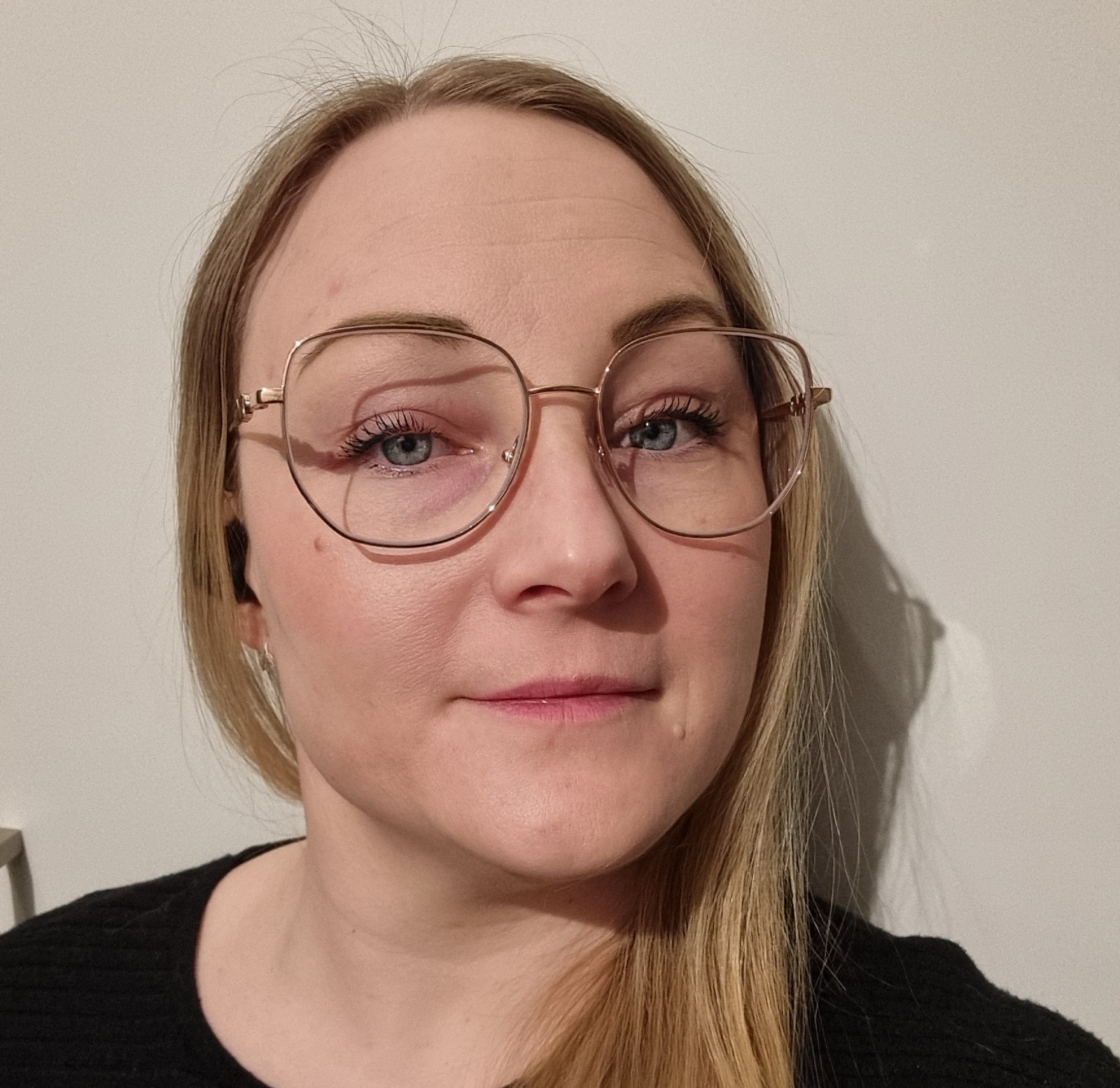 En profilbild på en blond kvinna i glasögon och svart stickad tröja